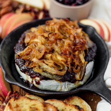 baked brie with fig jam in a cast iron skillet topped with caramelized oonion