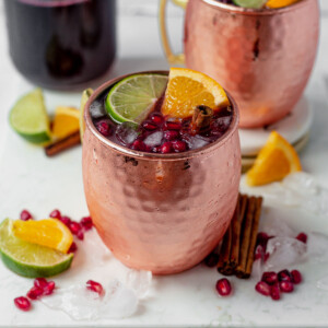cranberry moscow mule in a copper mug garnished with fresh lime and orange wedges