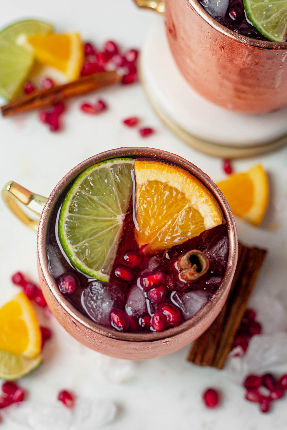 overhead shot of cranberry moscow mule in a copper mug with pomegrantes, lime wedge and orange wedge
