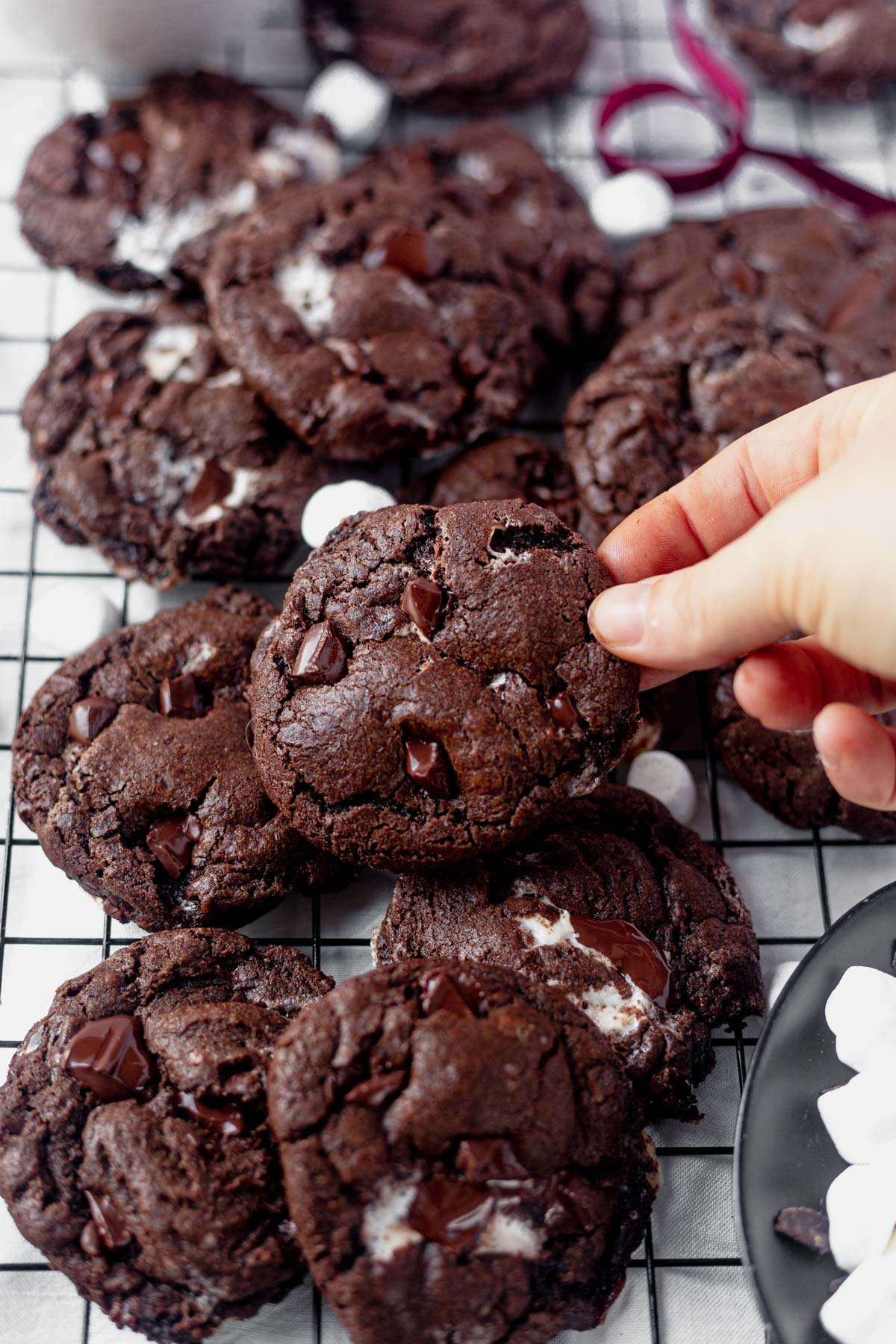 a hand picking up a chocolate chip marshmallow cookie from a pile