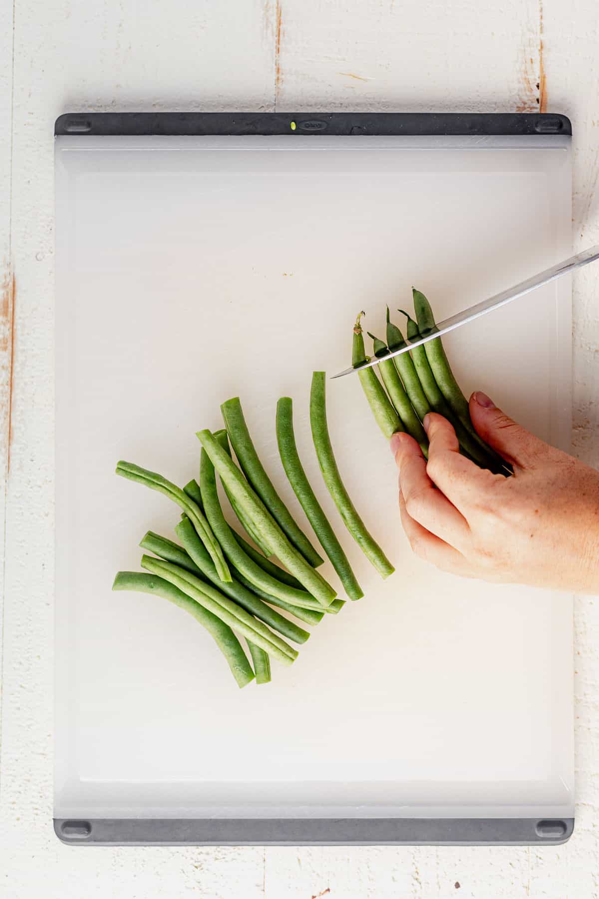 cutting the ends off of green beans on a cutting board.