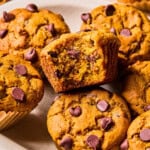 a tray of gluten free pumpkin muffins with tall bakery tops. One has a bite missing to see the melted chocolate chips and super soft center.