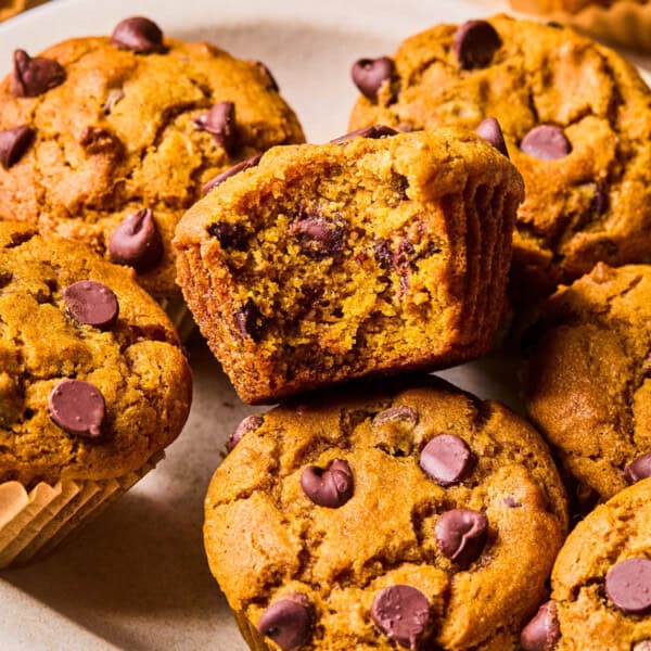 a tray of gluten free pumpkin muffins with tall bakery tops. One has a bite missing to see the melted chocolate chips and super soft center.