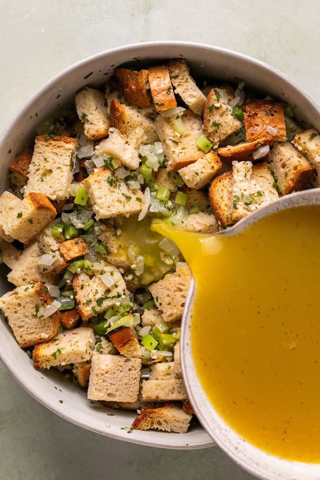 pouring broth and eggs over gluten-free stuffing mixture.