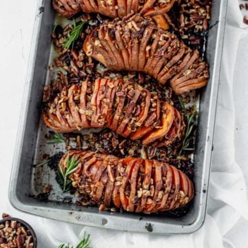 roasted hasselback sweet potatoes in a baking dish topped with brown sugar pecans and rosemary