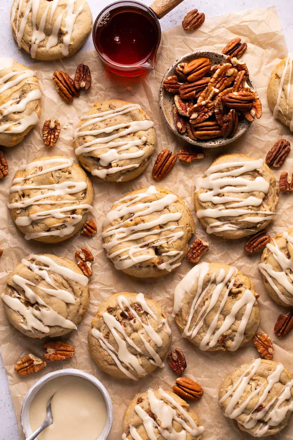 maple pecan cookies on a piece of parchment paper with maple icing drizzled on top.