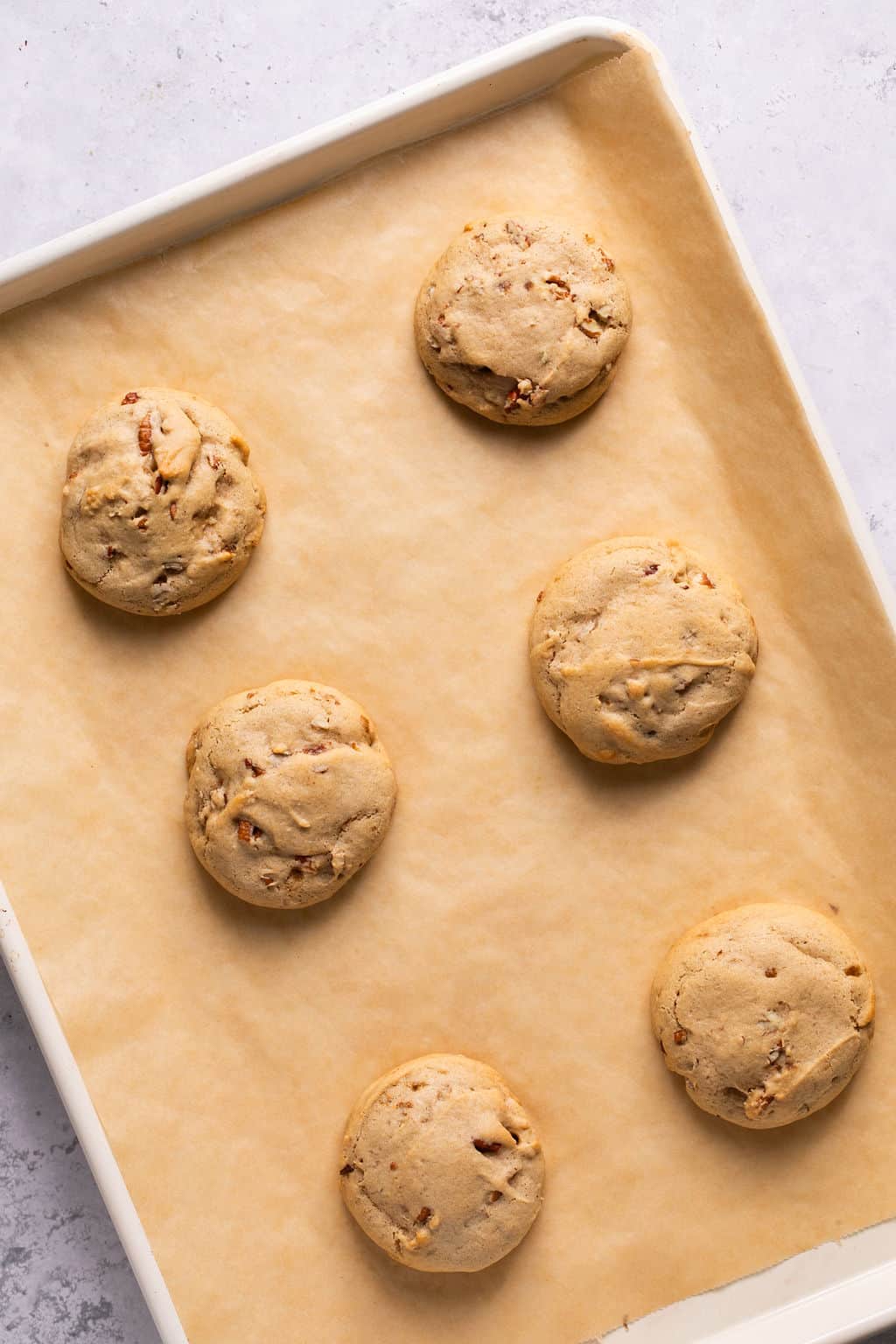 freshly baked maple pecan cookies cooling on a baking sheet.