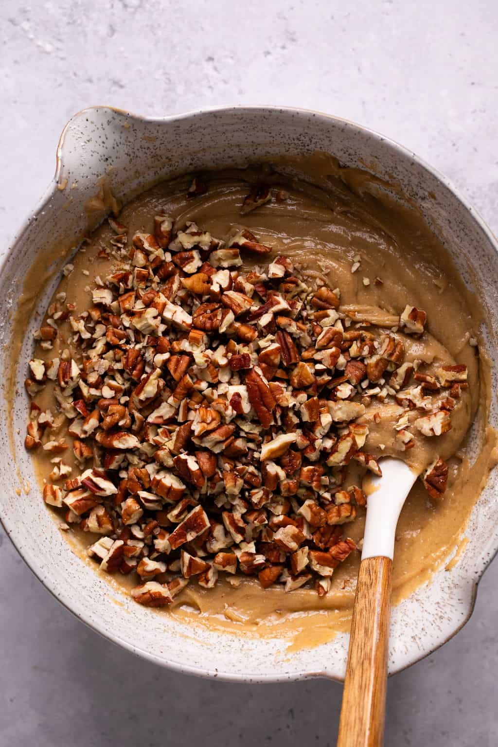 chopped pecans on top of maple cookie dough in a mixing bowl.