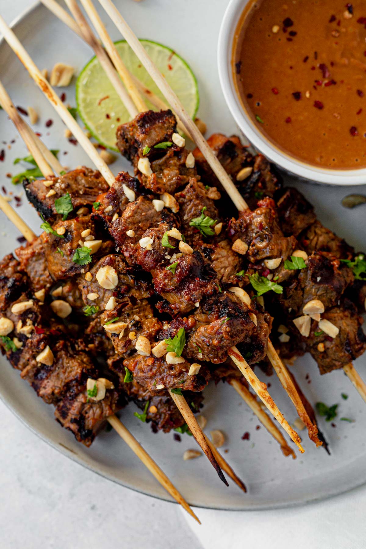 beef satay cooked with grill marks and topped with cilantro and peanuts next to thai peanut sauce