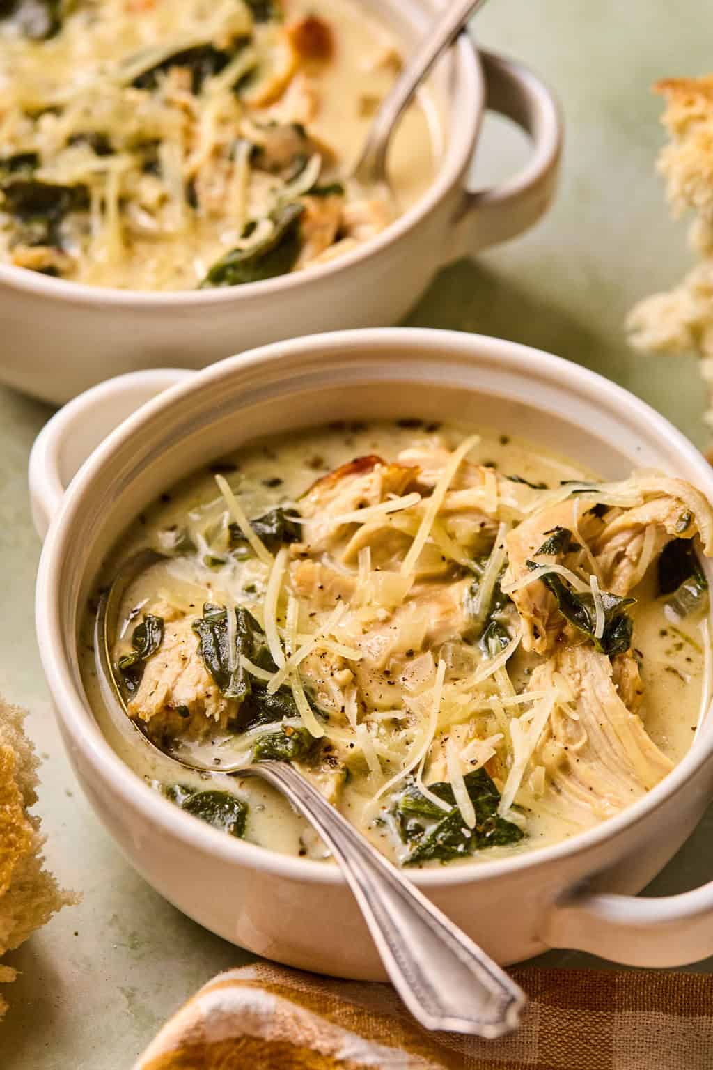 two bowls of chicken florentine soup with a spoon in it.