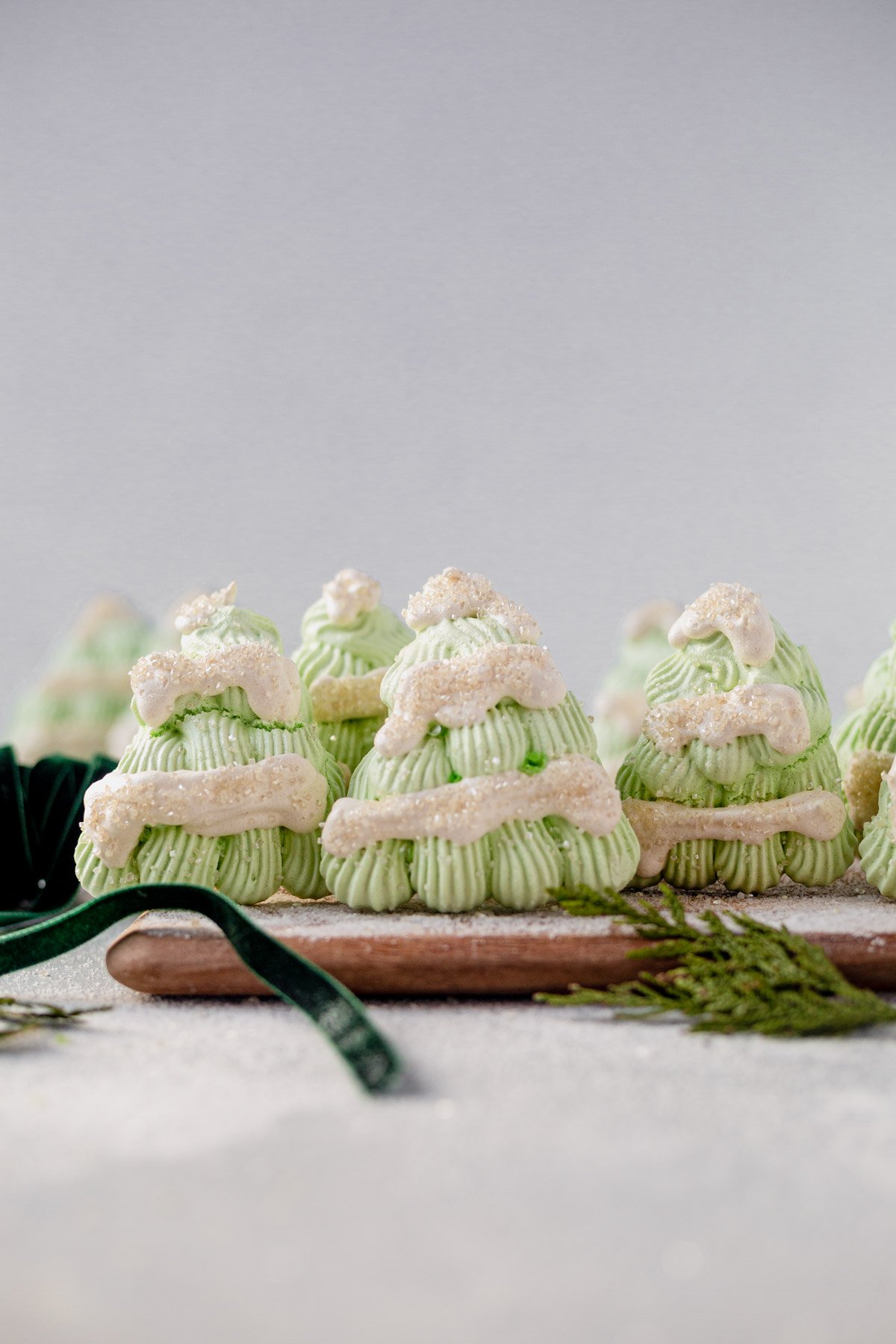 6 christmas tree merginues standing up on a white table with fresh greenery around it