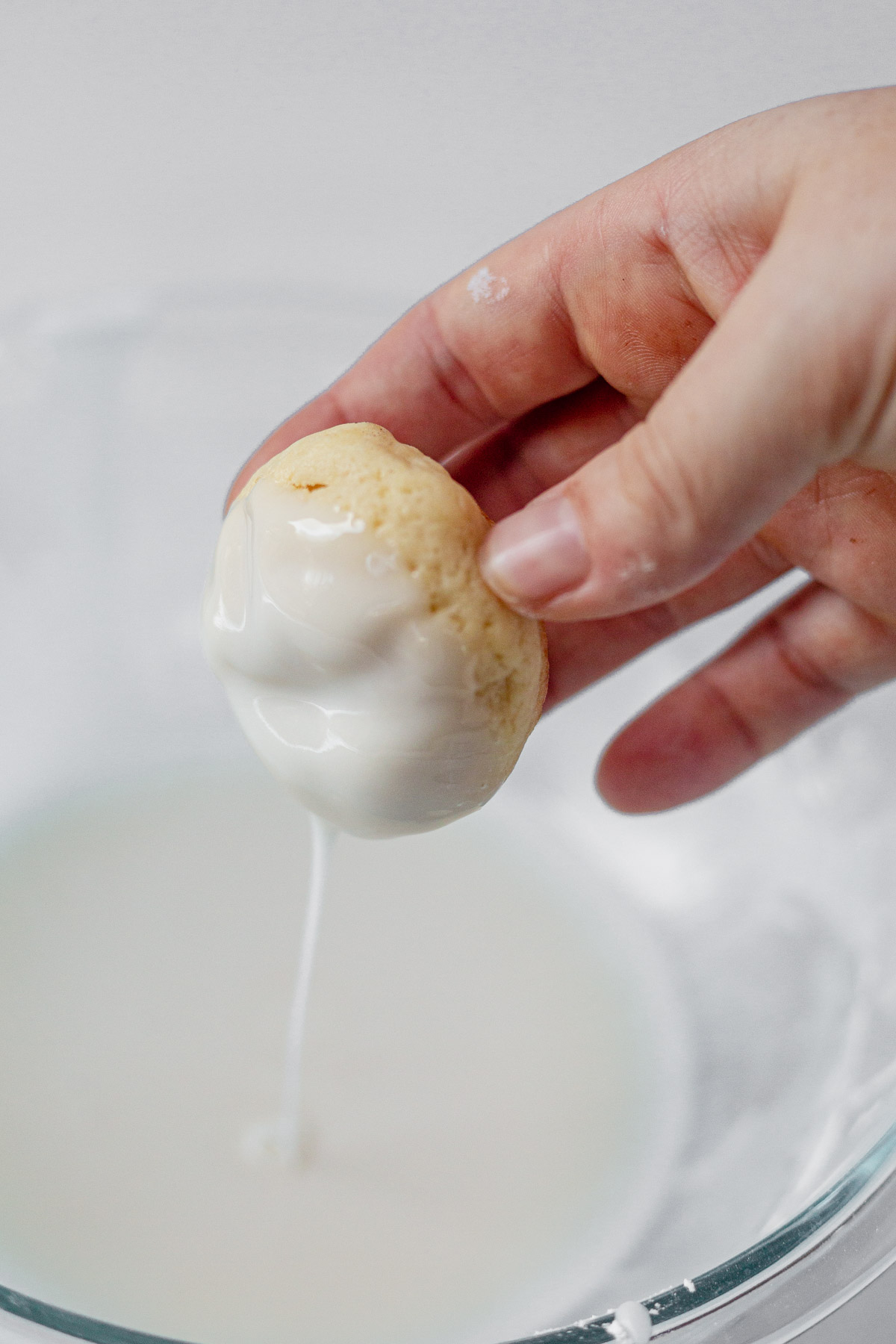 a hand dunking an Italian cookie into glaze