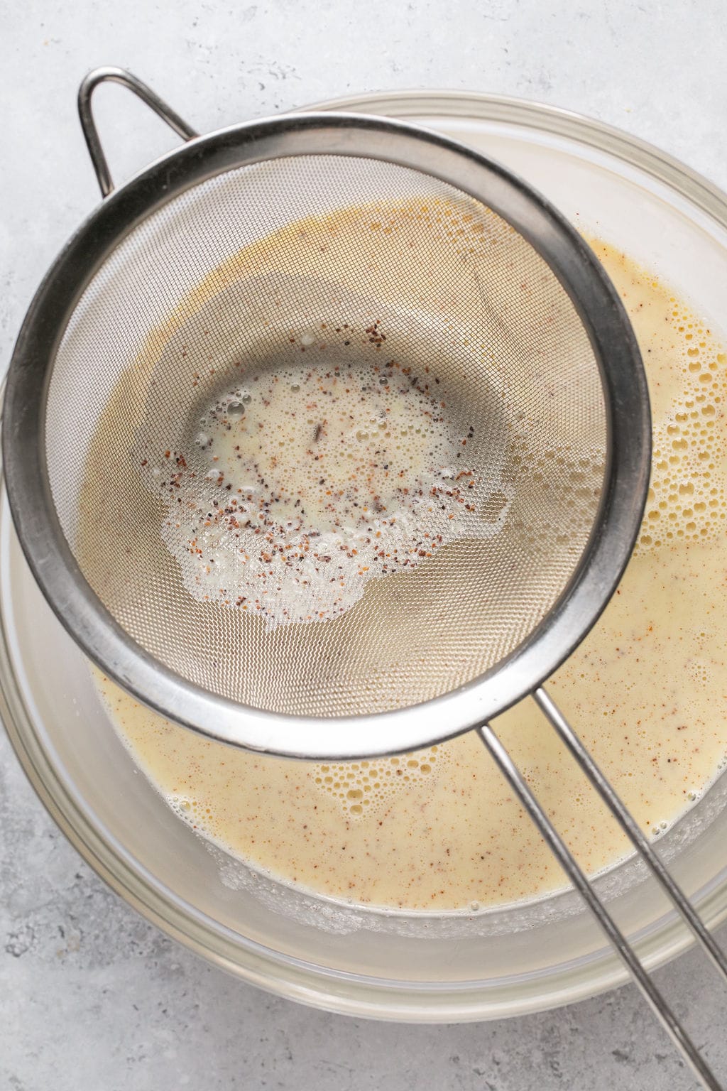 straining homemade dairy free eggnog into a bowl.