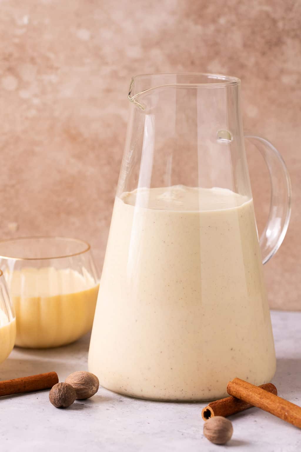 a pitcher of dairy free eggnog on the counter with two serving glasses.