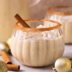 a glass of dairy free eggnog with whipped cream and a cinnamon stick.