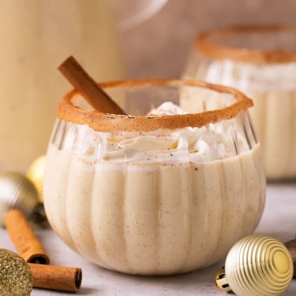 a glass of dairy free eggnog with whipped cream and a cinnamon stick.