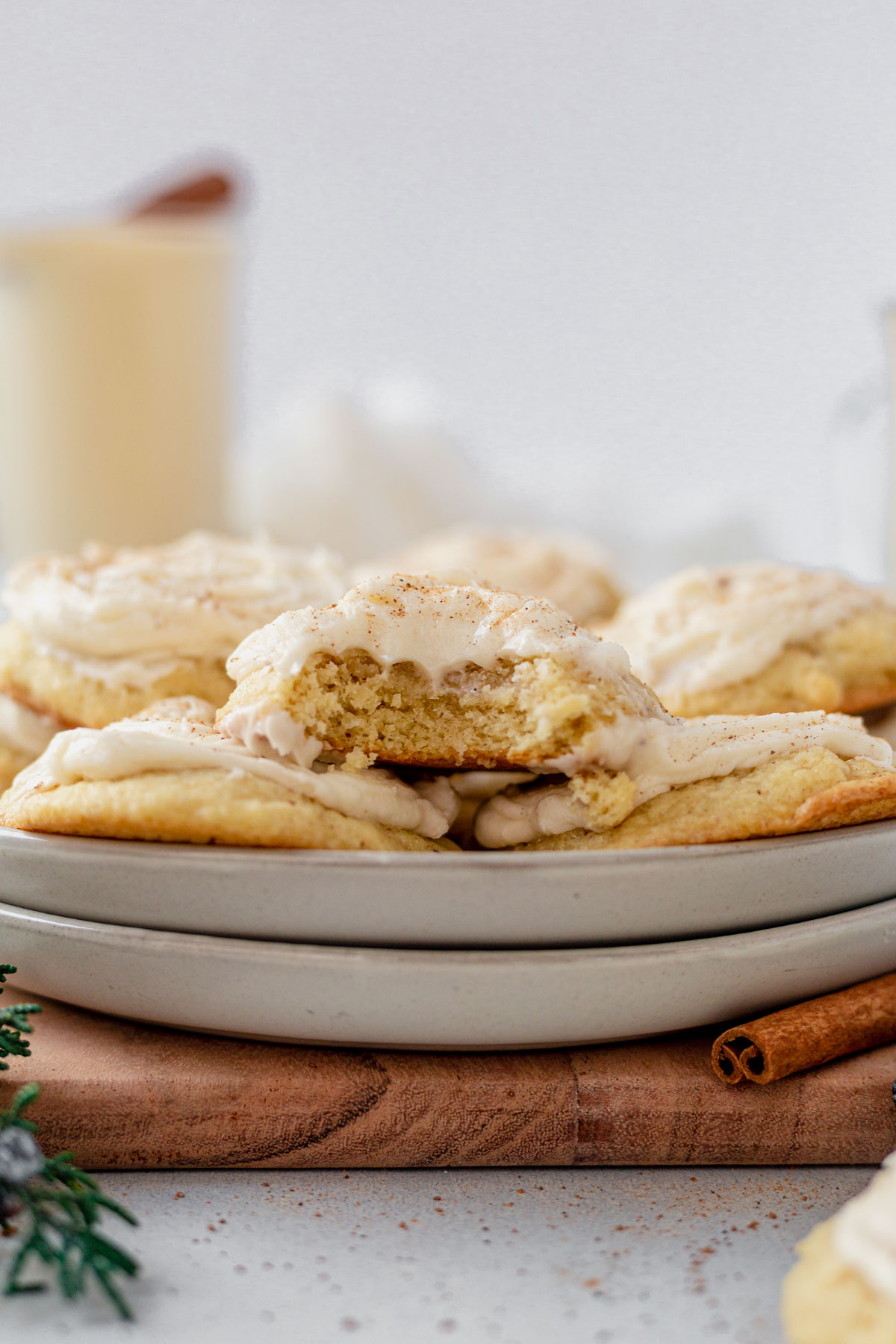 frosted eggnog cookies stacked on a white plate with a bite taken out of one to see the soft center
