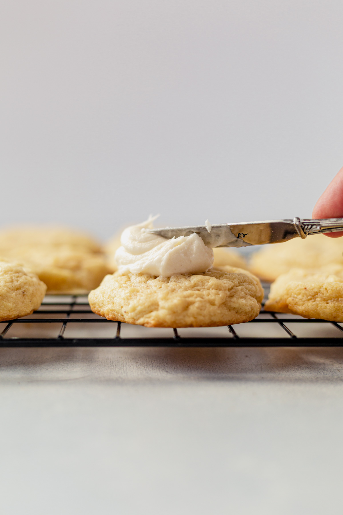 a knife spreading cream cheese frosting on top of an eggnog cookoie