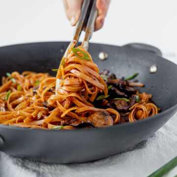 tongs twirling gochujang noodles in a wok
