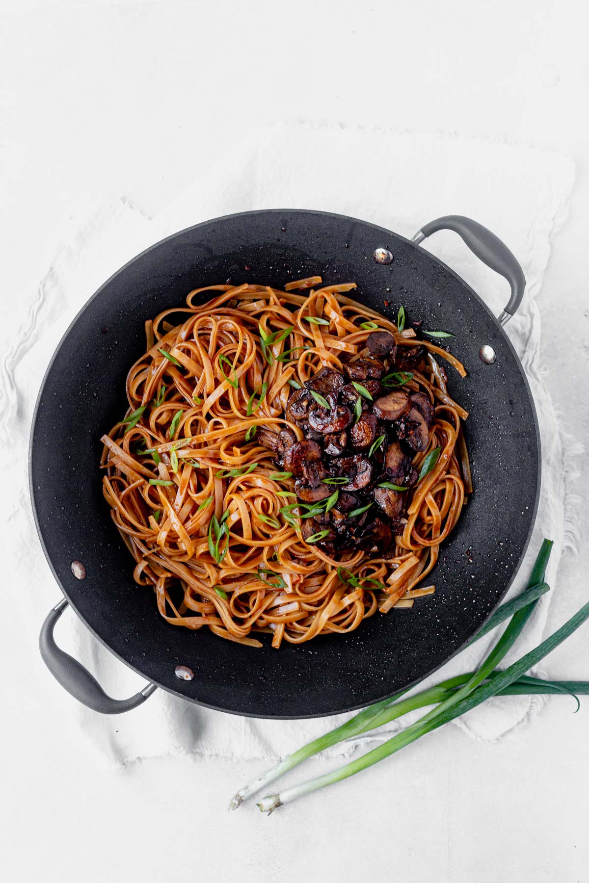 gochujang noodles in a wok with mushrooms and green onion
