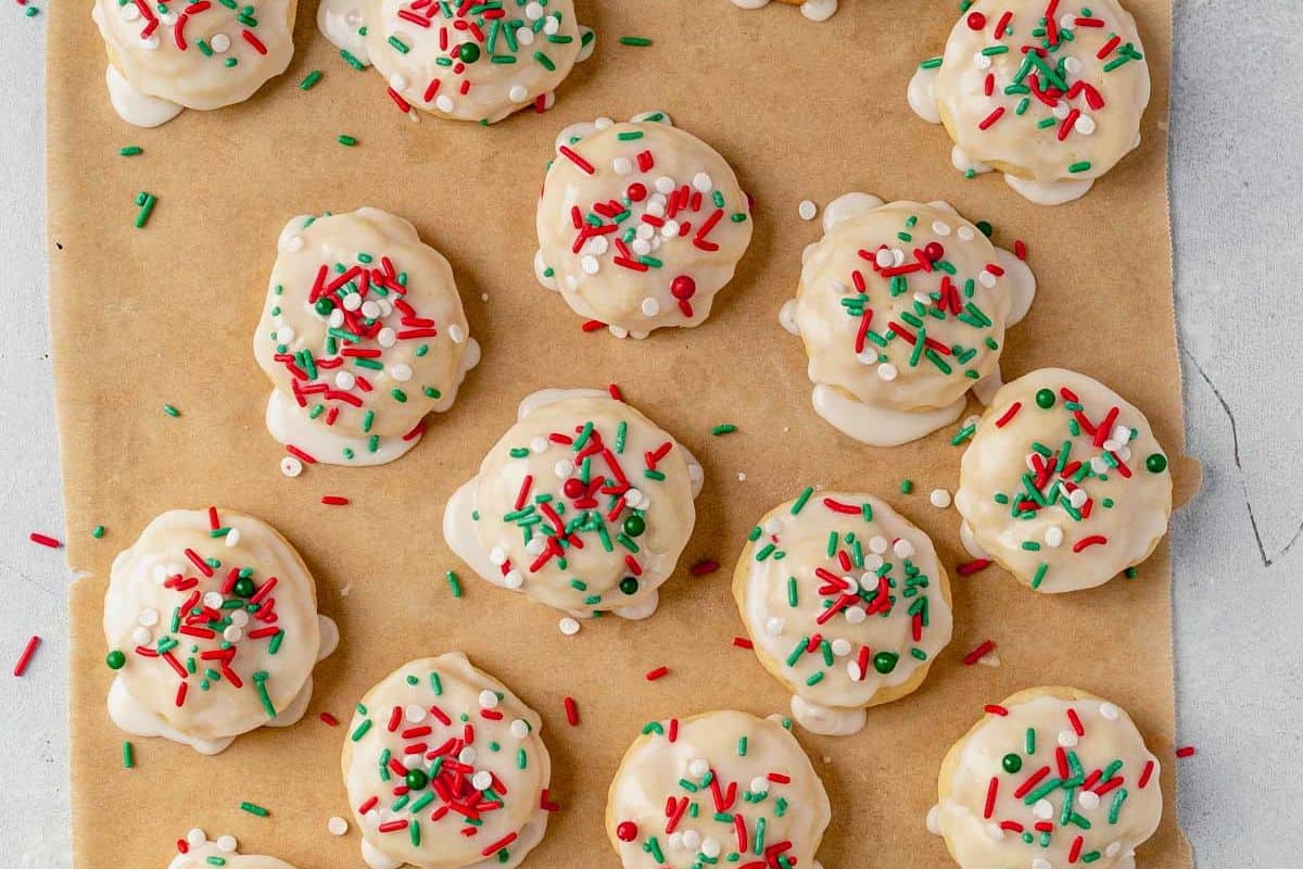 freshly baked italian sprinkle cookies on parchment paper with wet icing and sprinkles
