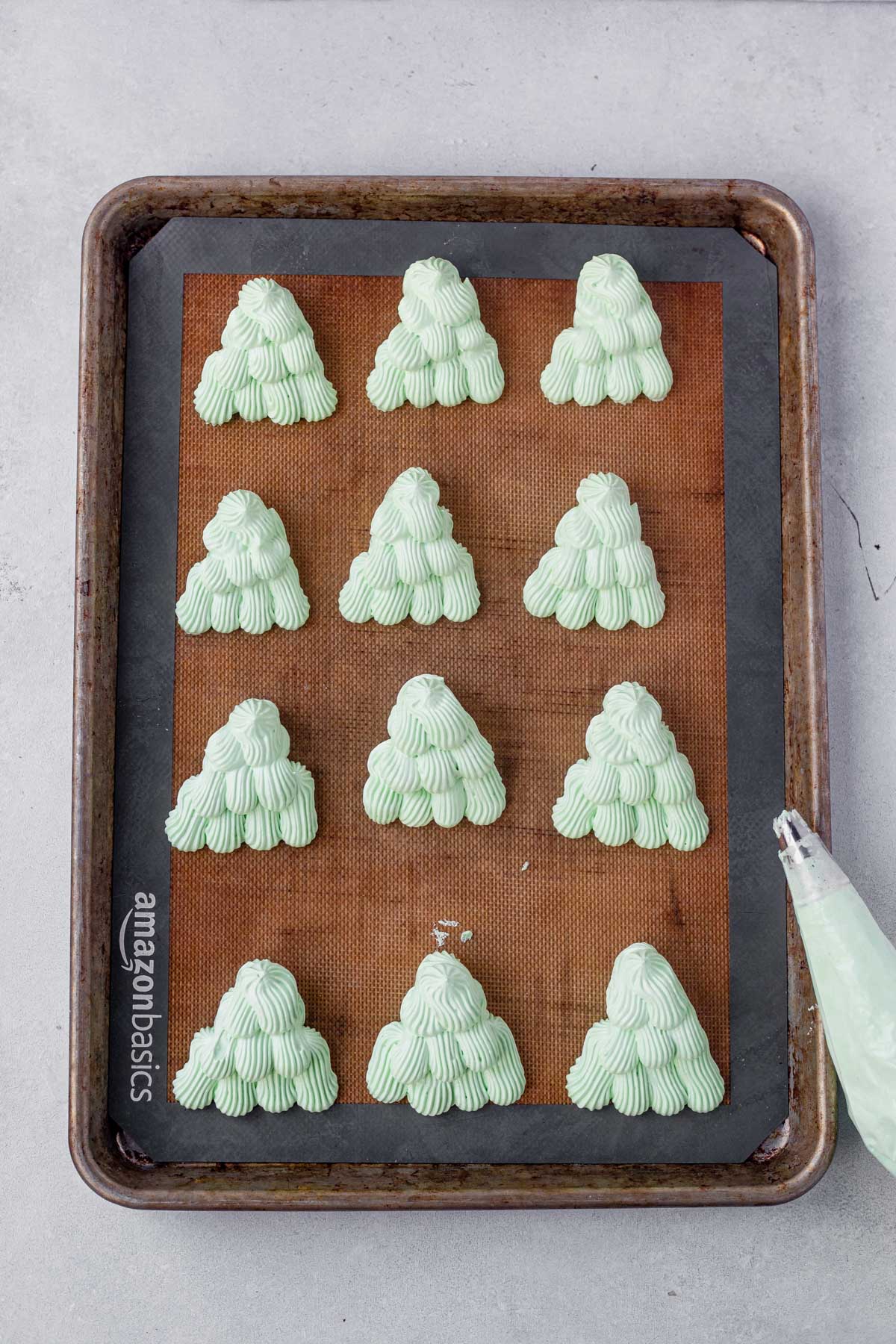 12 meringue christmas trees piped on a baking sheet