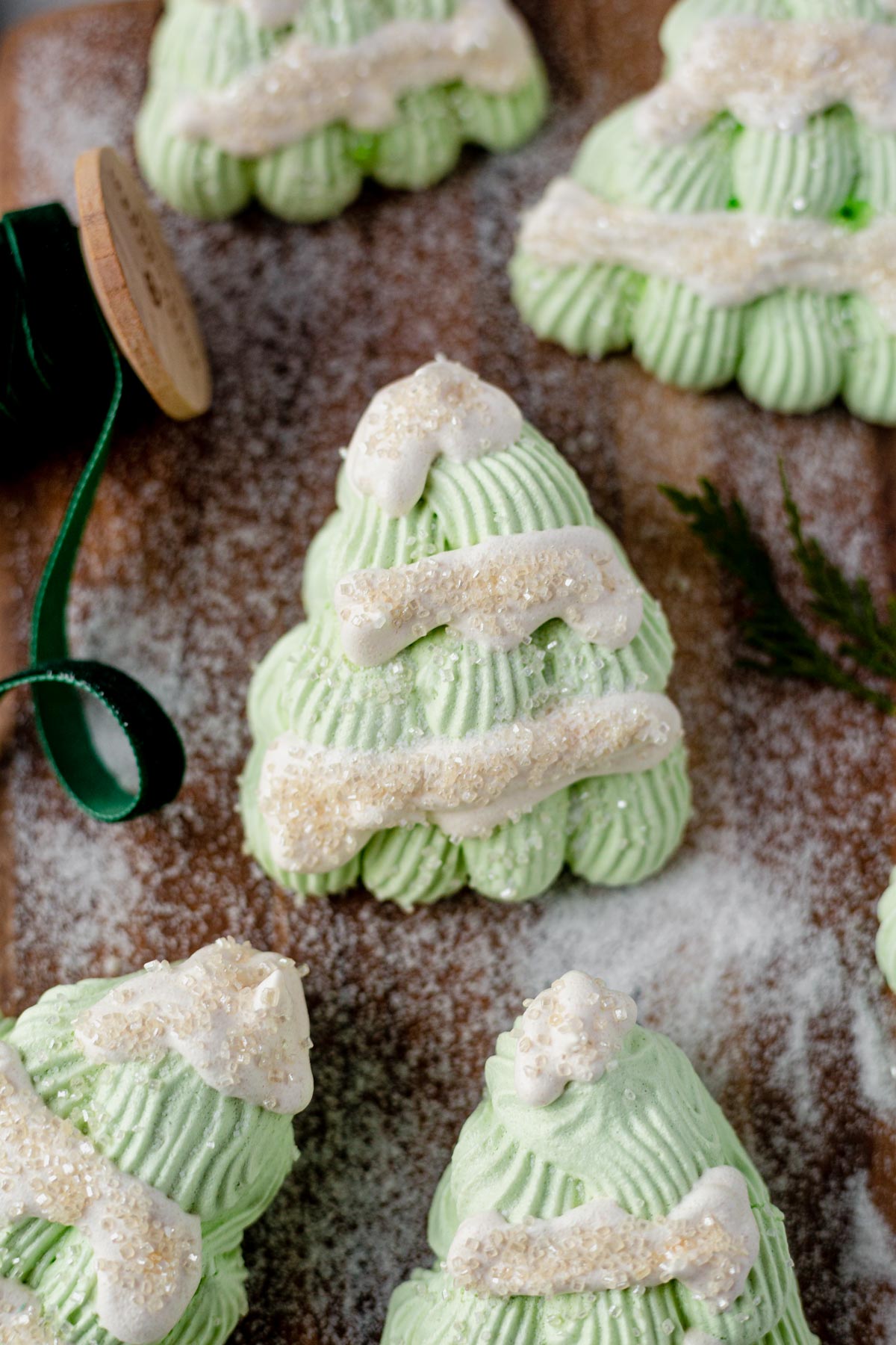 meringue christmas trees on a wood serving board with granulated sugar and green ribbon surrounding them