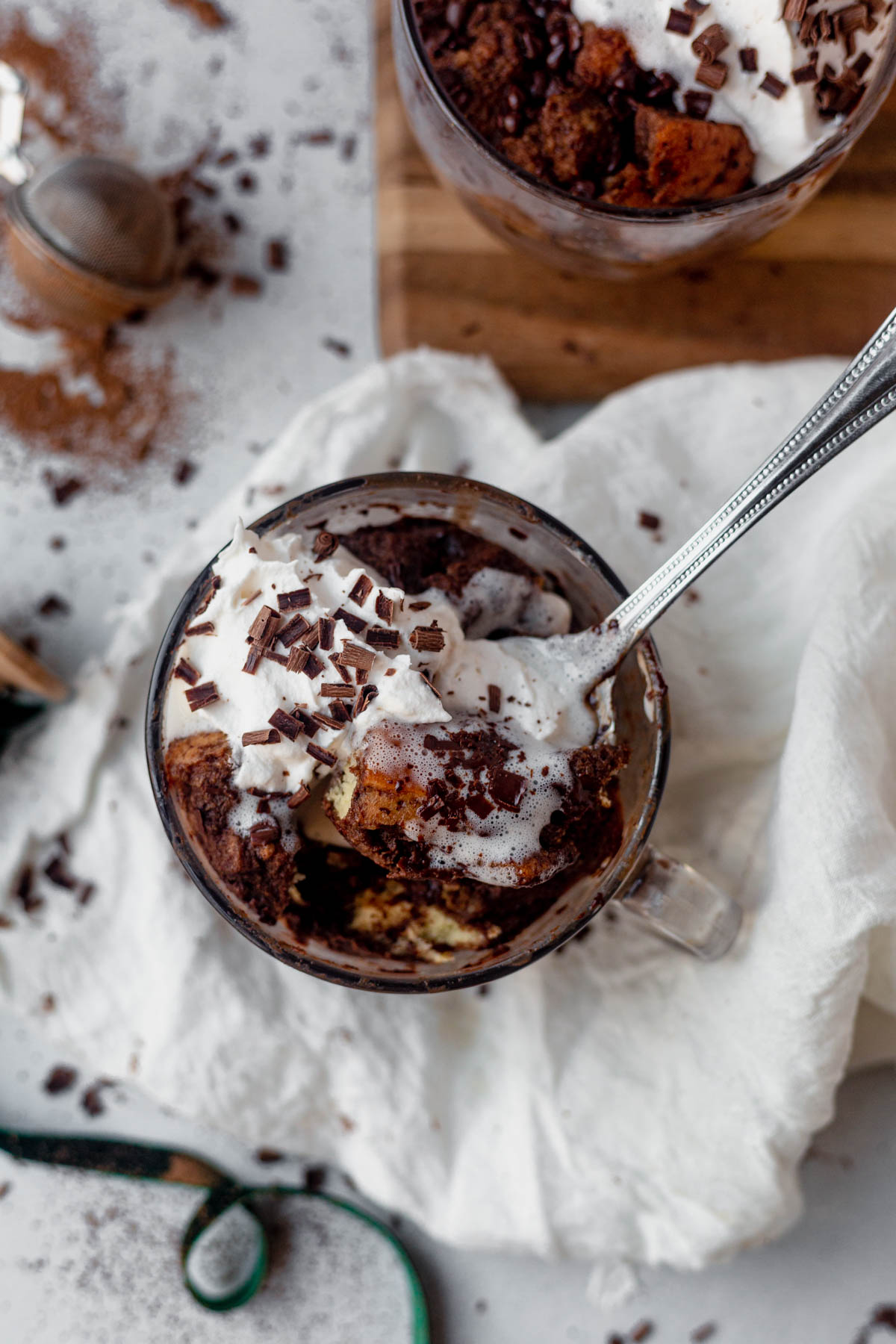 a spoon scooping out a bite of chocolate microwave bread pudding with whipped cream on top