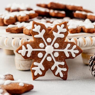 a gingerbread snowflake cookie with royal icing leaning against a cake stand