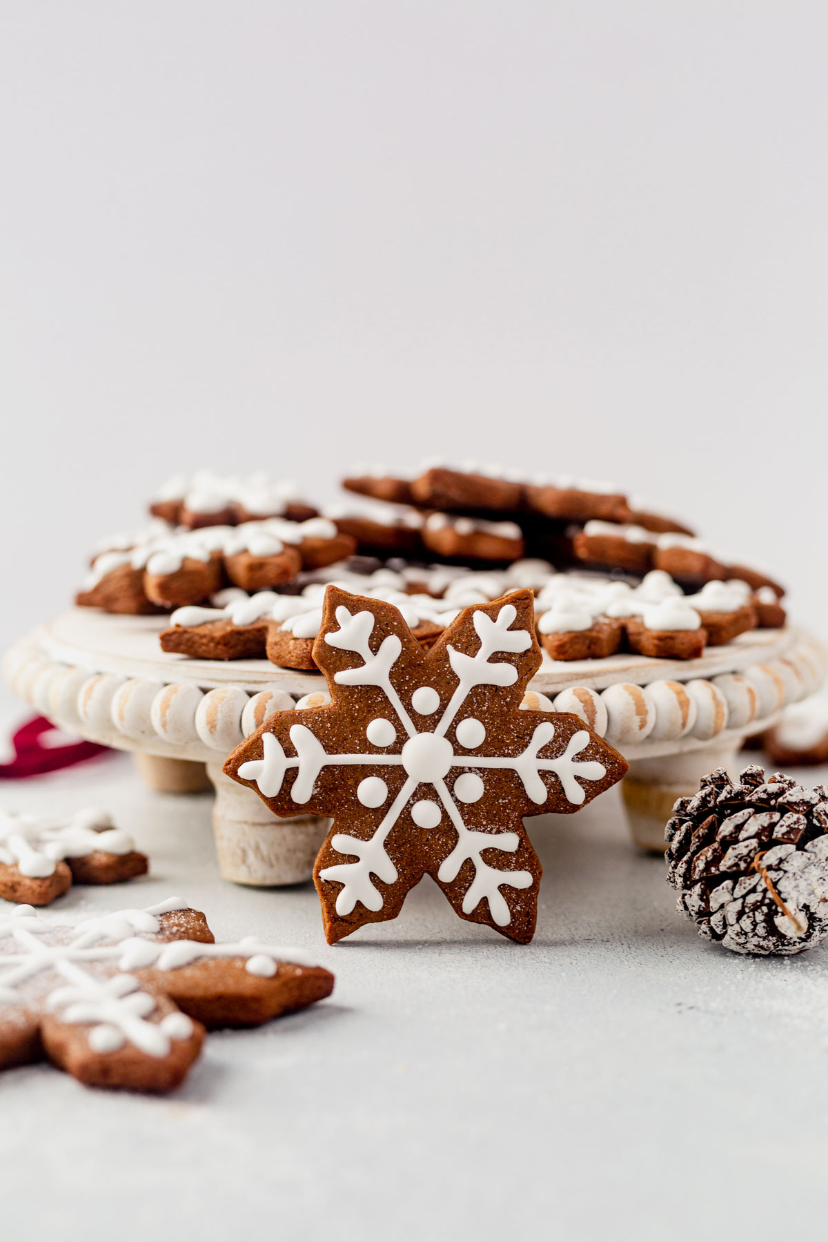a snowflake cookie decorated with royal icing standing up against a cake stand