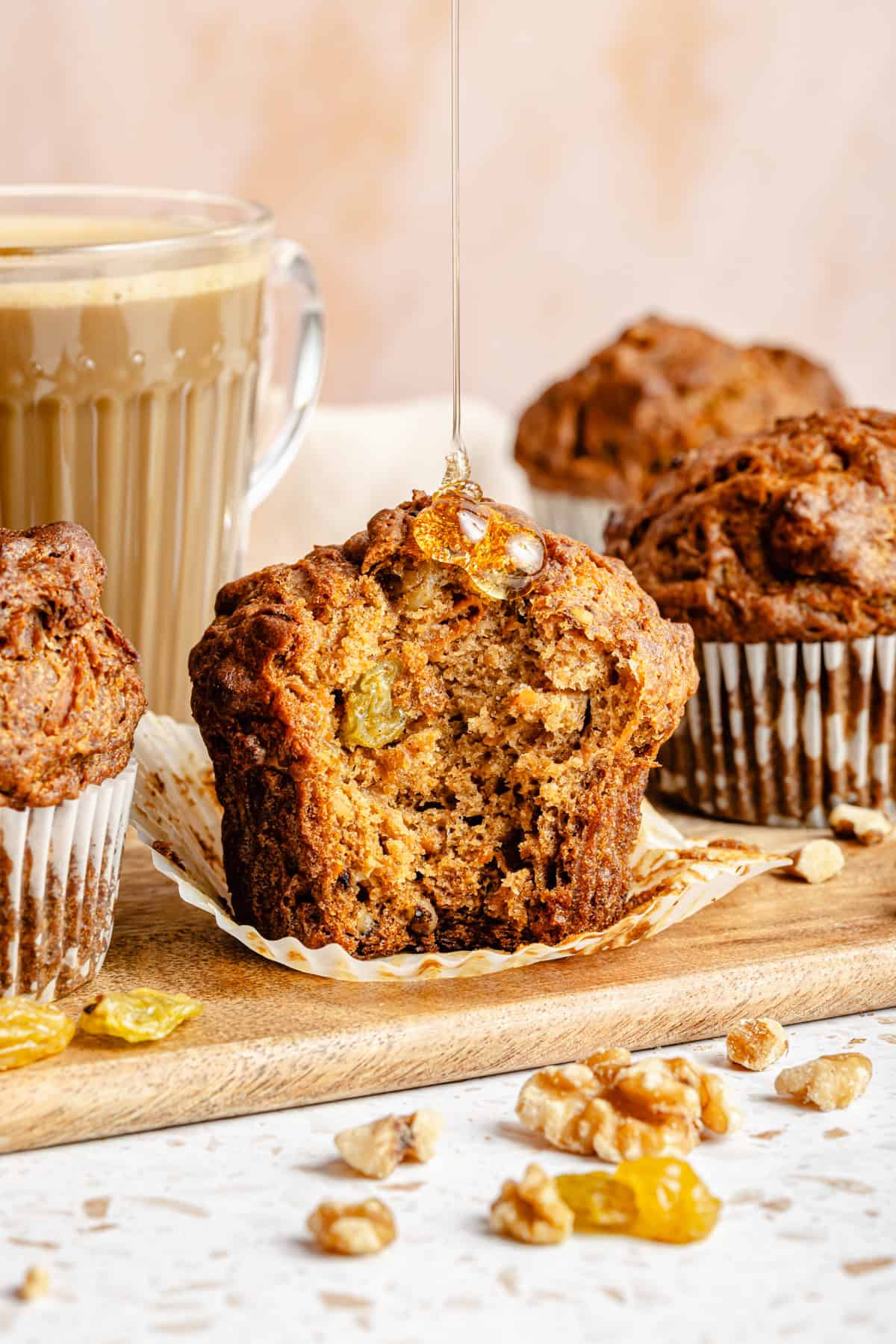 a morning glory muffin on a serving board with a bite taken out and a drizzle of honey on top.