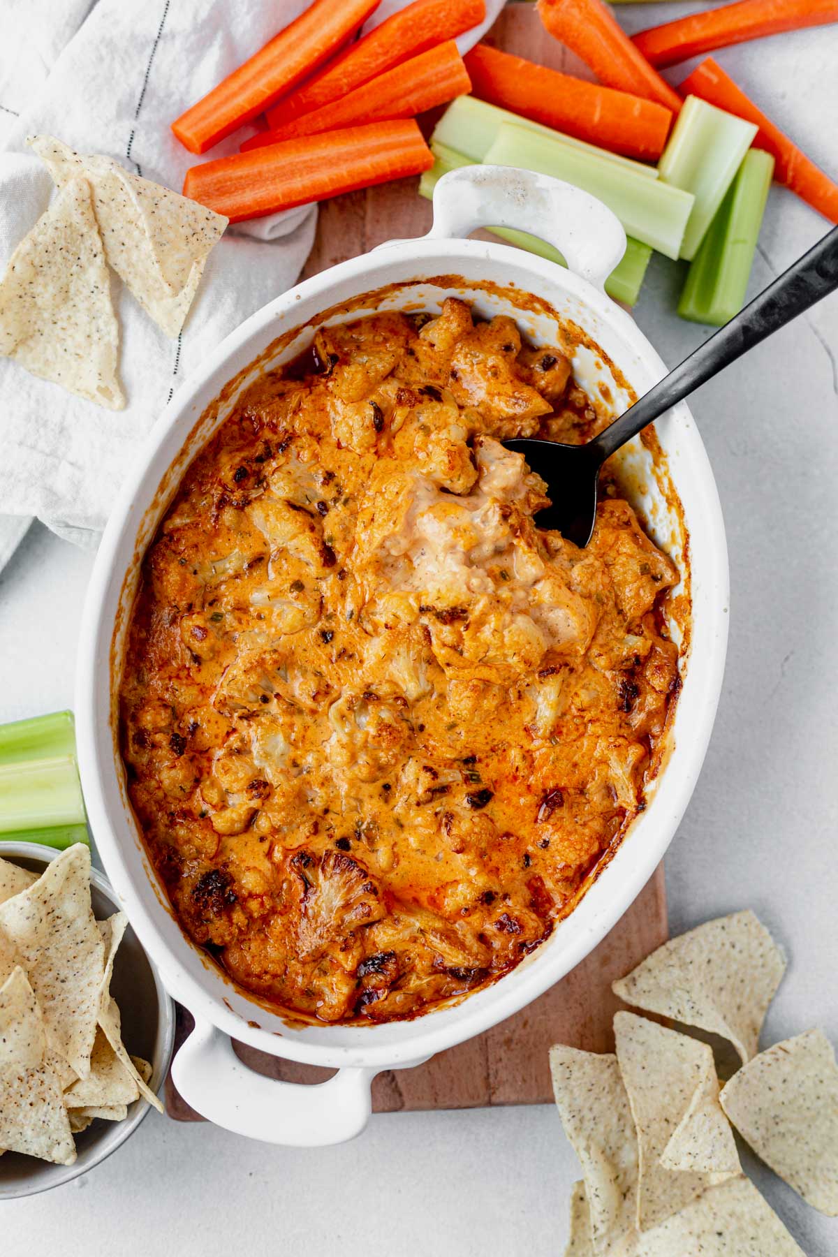 buffalo cauliflower dip in a baking dish with celery and carrot sticks