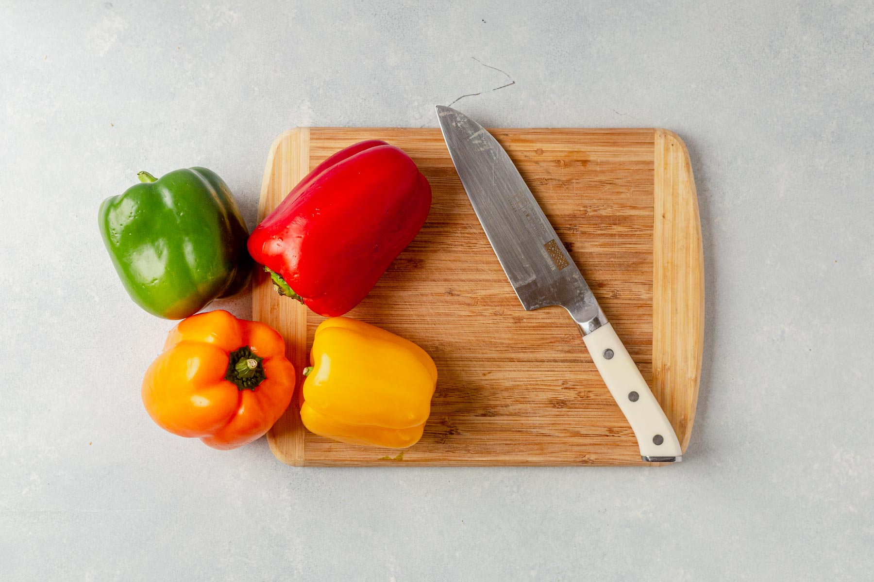 four bell peppers on a cutting board with a knife