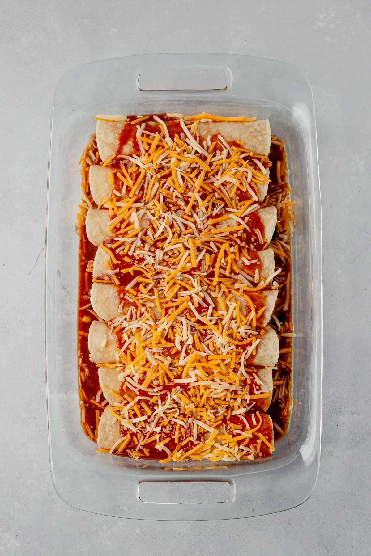 rolled enchiladas in a baking dish with cheese before baking