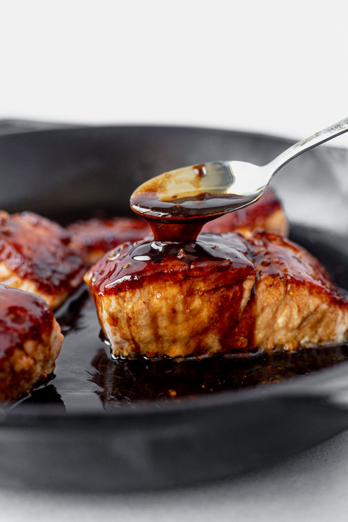 spooning teriyaki glaze over a piece of cooked salmon