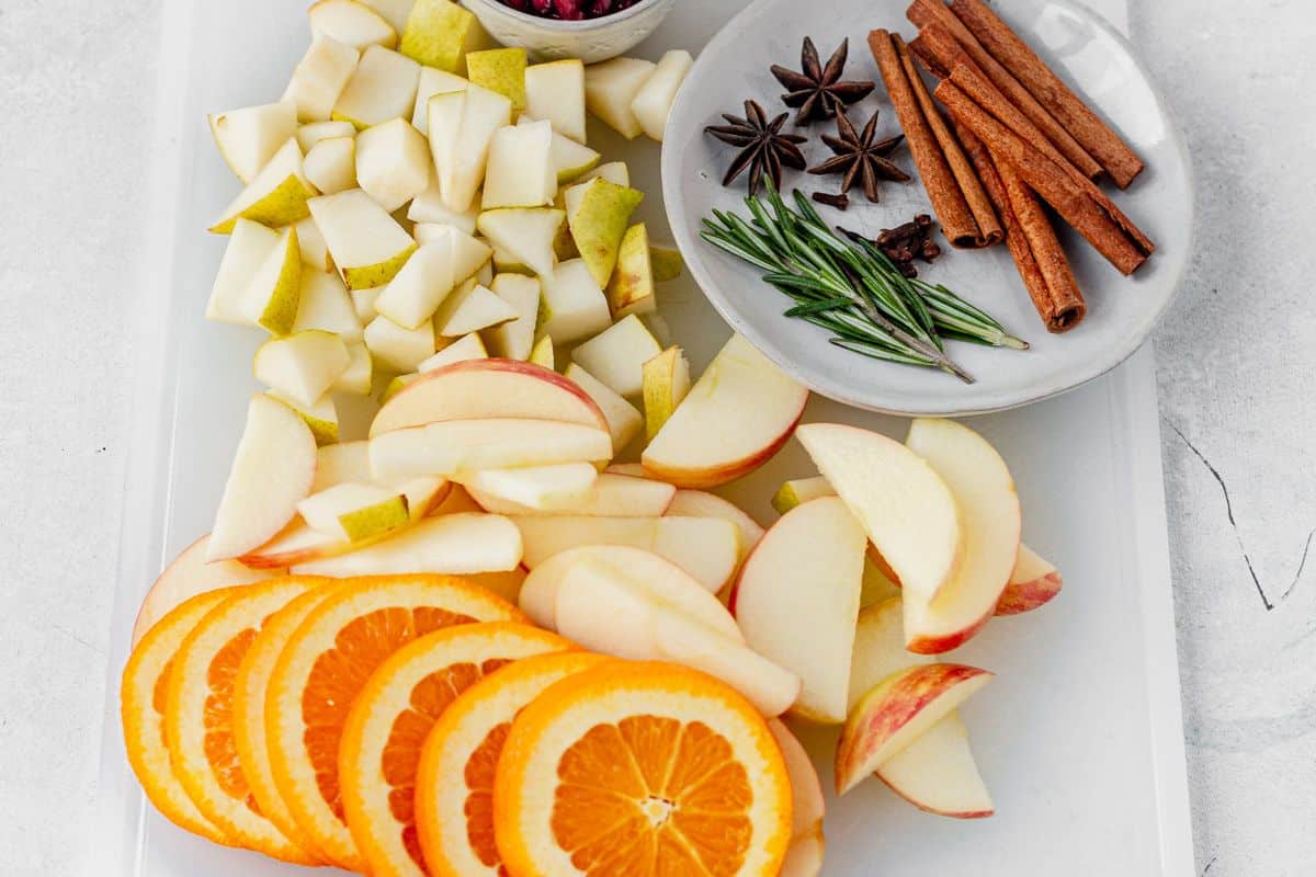 sliced oranges, sliced apples, sliced pears, cinnamont sticks, and rosemary on a cutting board