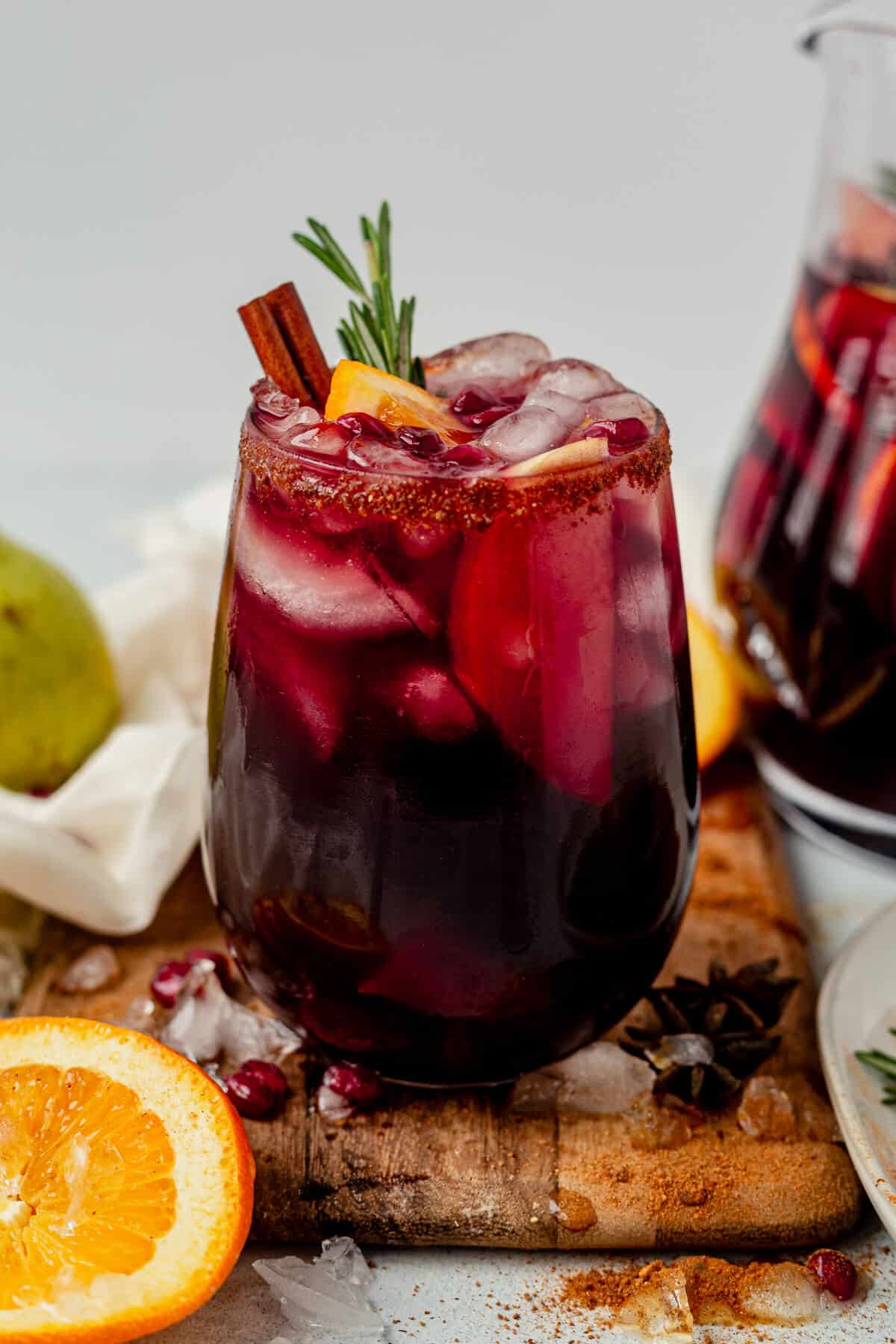 a glass of red winter sangria with cinnamon sugar rim, fresh fruit, and rosemary
