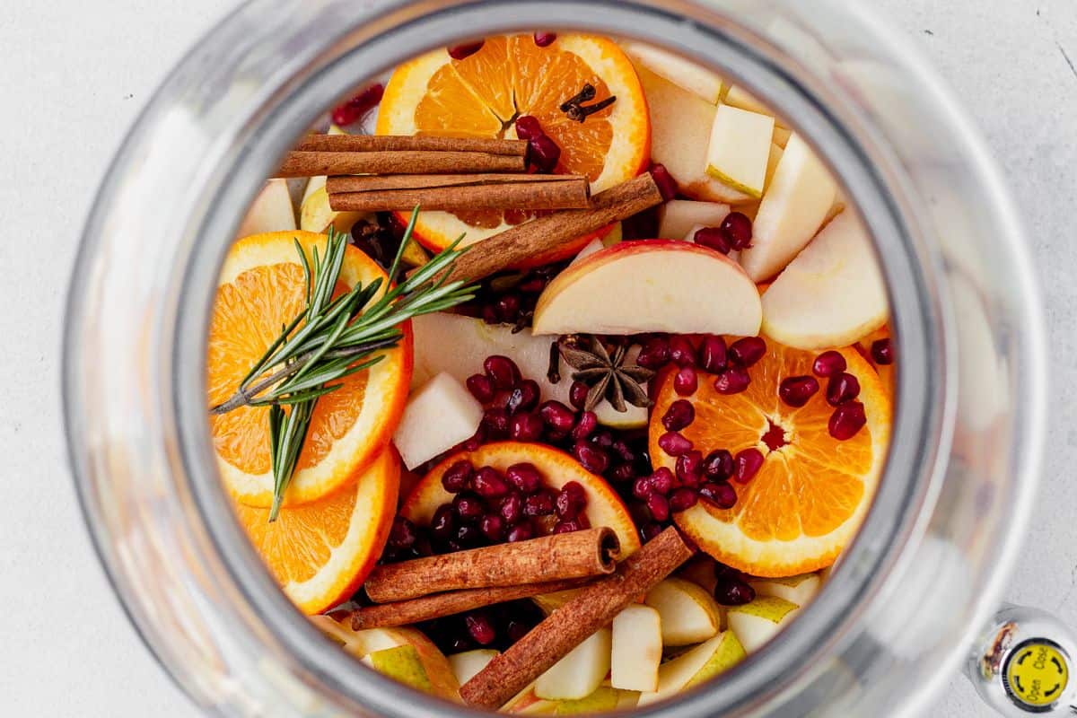 apples, oranges, pears, rosemary, and cinnamon in a pitcher
