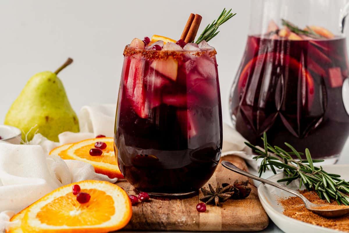 red winter sangria in a wine glass and a pitcher of sangria next to it