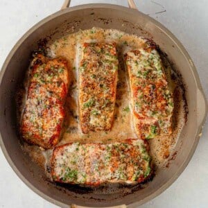 4 pieces of herb grilled salmon in a skillet with garlic herb butter on top