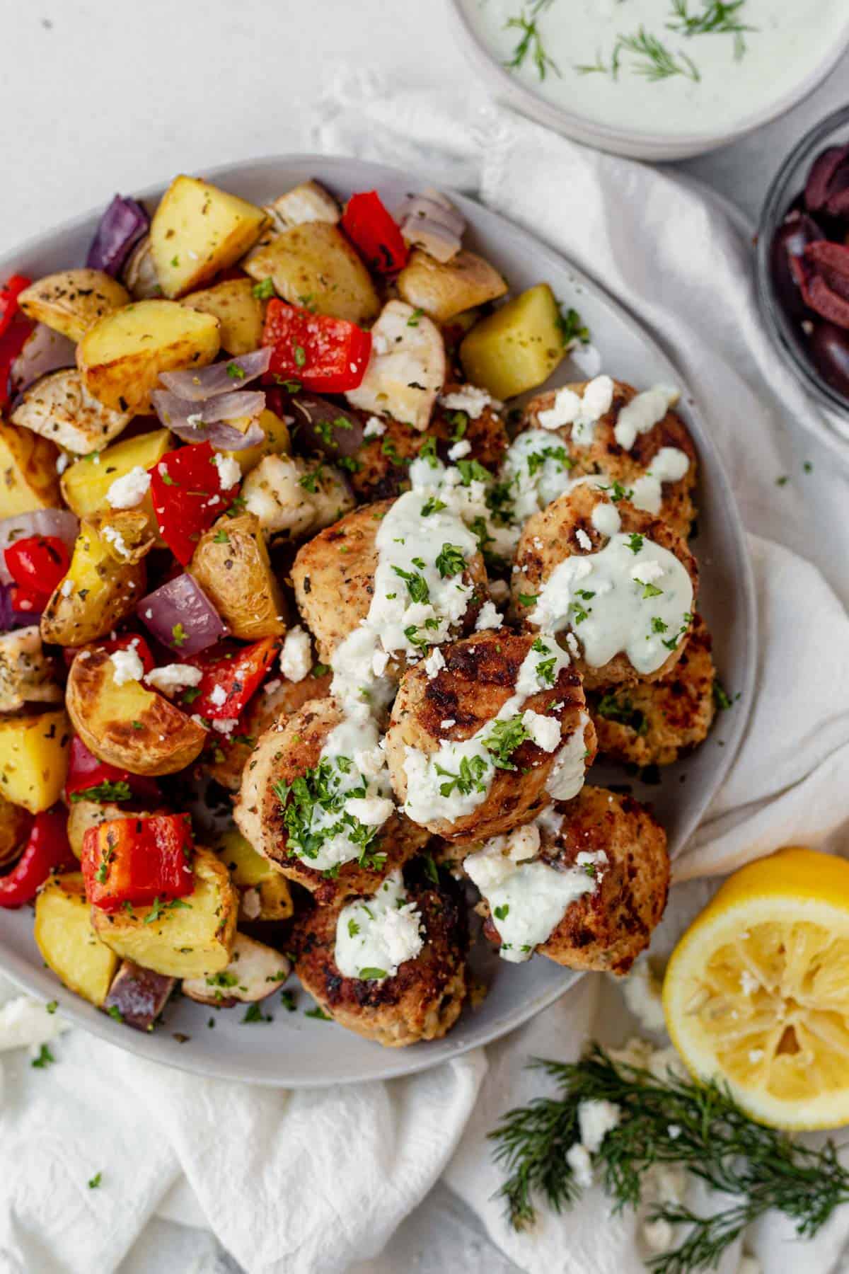 a plate of greek chicken meatballs with roasted vegetables and topped with tzatziki sauce