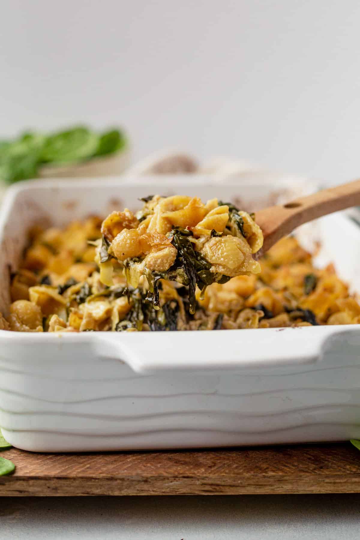 a wooden spoon with a scoop of spinach artichoke pasta bake