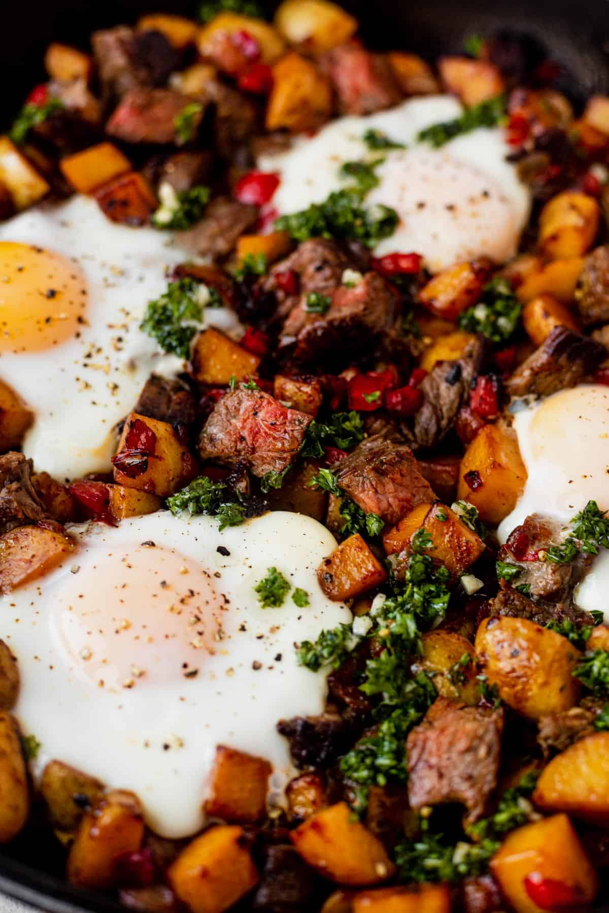 steak and potato breakfast hash in a skillet with fried eggs on top