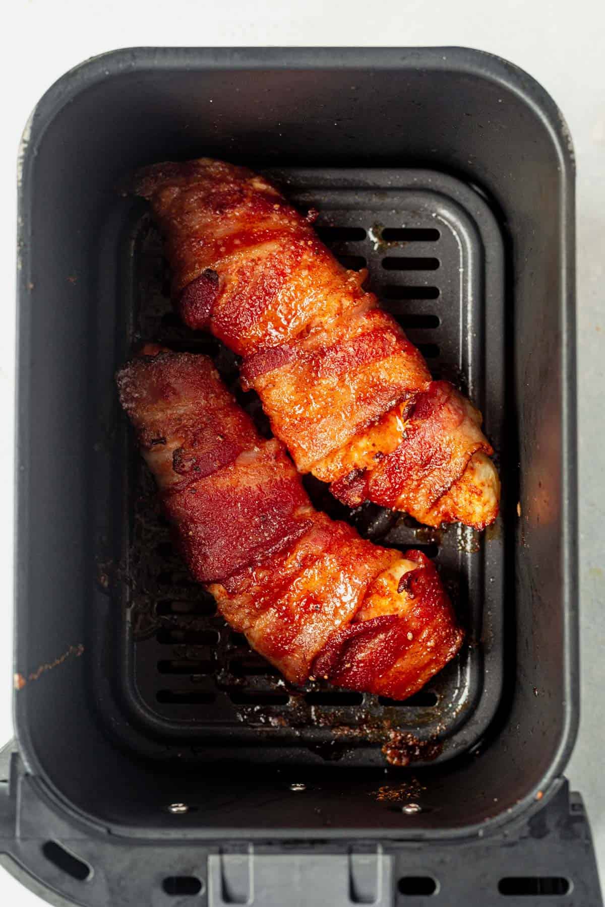 two bacon wrapped chicken breasts cooked and crispy in an air fryer basket