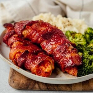 bacon wrapped chicken breast on a plate with potatoes and broccoli