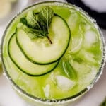 sliced cucumbers on top of a cucumber margarita in a glass.