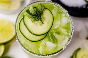 sliced cucumbers on top of a cucumber margarita in a glass.