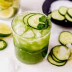 a cucumber margarita topped with cucumber slices and mint