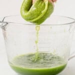 straining fresh cucumber juice through a nut milk bag into a glass bowl.