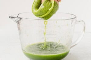 straining fresh cucumber juice through a nut milk bag into a glass bowl.